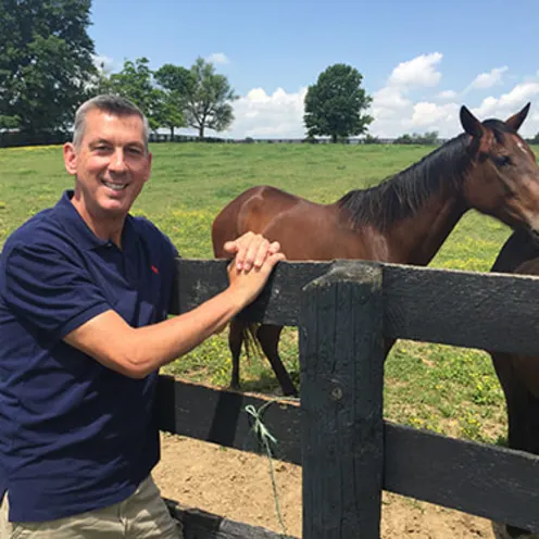 Dr. Browning, equine veterinarian, leaning on fence next to two brown horses
